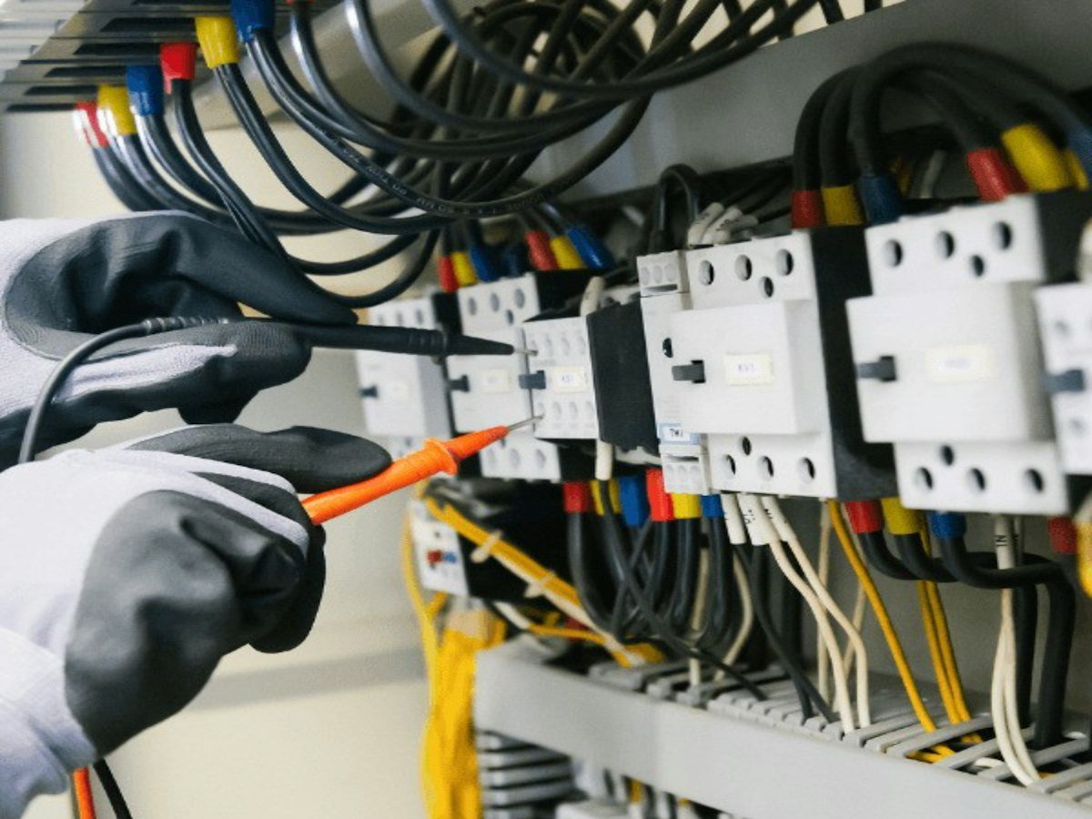 Technician testing contactors and wiring inside an electrical control panel.