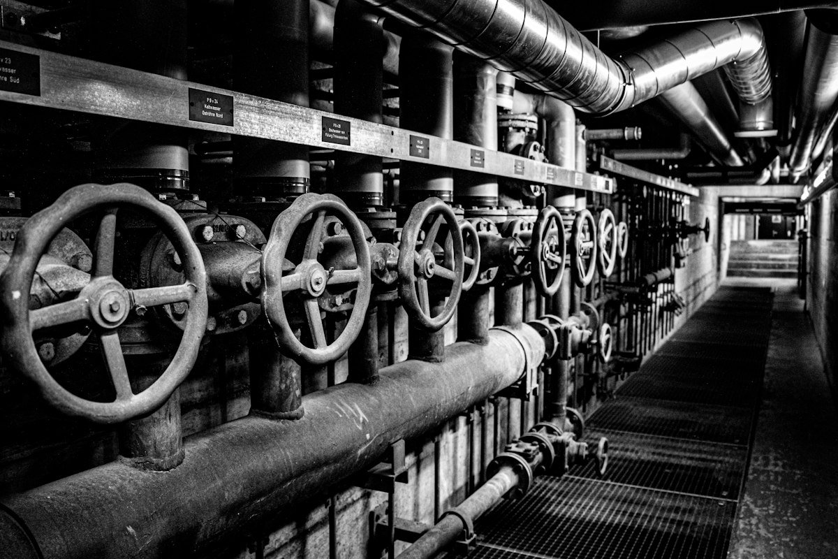 Row of industrial valves and pipework in a plant corridor.